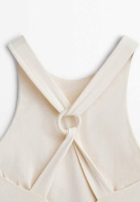 Tissu de couleur crème avec larges bretelles croisées dans le dos, reliées par un détail en anneau circulaire texturé.
