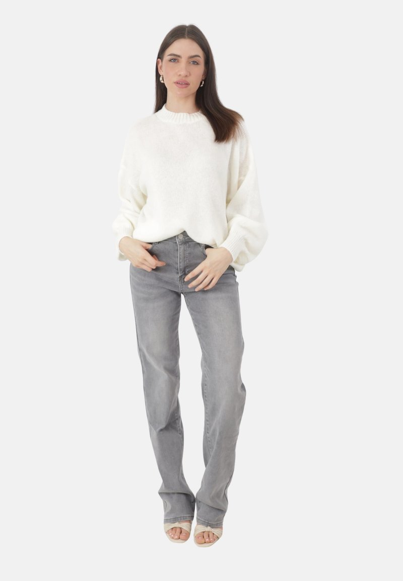 Weißer, strukturiert gestrickter Pullover mit einem gerippten Halsausschnitt, kombiniert mit hellgrauen, geraden Jeans und beigen Sandalen mit Riemchen.