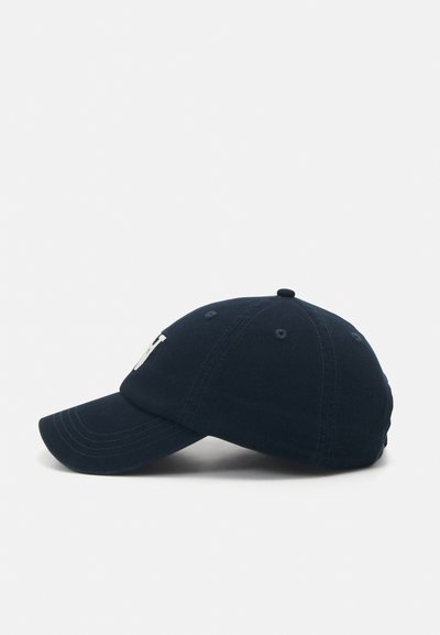 Navy blue cotton baseball cap with curved visor, six-panel design, and embroidered white logo on the front. Textured fabric visible.