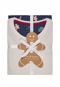 Twee sets damespyjama's, één crème en één marineblauw met feestelijke patronen, samengebonden met een wit lint en een label in de vorm van een speculaas.