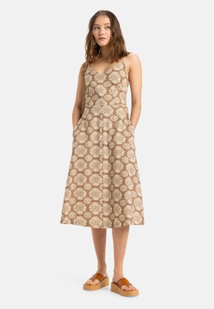 Braunes Midi-Kleid mit weißem Blumenmuster, Spaghettiträgern und seitlichen Taschen. Stylisch kombiniert mit braunen Plateausandalen.