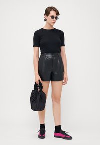 Svart kortärmad topp, högmidjade svarta lädershorts, svart kuvertväska och rosa-svarta sneakers med texturerade detaljer.