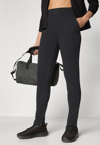Sorte treningsleggings med en glatt tekstur, tettsittende design og elastisk midje. Kombineres med en svart duffelbag og svarte joggesko.
