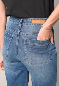 Jeans en denim bleu avec une taille mi-haute, dotés de deux poches arrière et d'une étiquette de marque en cuir au niveau de la taille. Fini de tissu texturé.