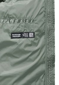 Gevoerde groene jas van materiaal met een soepele textuur, met elastische plooidetails en een zwart label met een QR-code aan de onderkant.