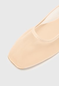 Beige ballerina med fyrkantig tå, tillverkad av texturerat tyg. Har en slät foder och minimal sömnad längs kanten.