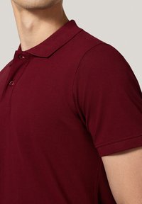 Burgundowa koszulka polo z miękkiego, teksturowanego materiału, z klasycznym kołnierzykiem, trzema guzikami i krótkimi rękawami.