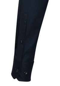 Polsino della camicia a maniche lunghe della marina con due bottoni neri rotondi, texture sottile e emblema ricamato a forma di rosa vicino alla pattina dei bottoni.