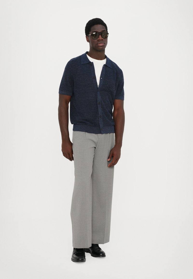 Navy short-sleeve cardigan over a white t-shirt, paired with light gray wide-leg trousers and black shoes. The cardigan features a button closure.