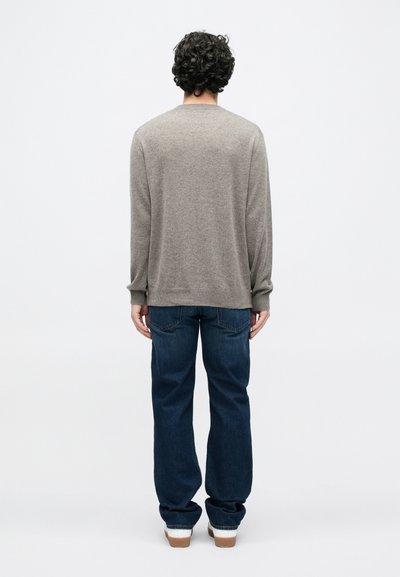 Hall helekampsest villasest kampsunist, millel on ümmargune kaelus, lõdvestunud lõige ja pikad varrukad, mida on kombineeritud tumesiniste teksapükste ja valgete tossudega.