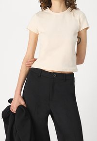 Short-sleeved cream t-shirt made of ribbed fabric, featuring a rounded neckline and a cropped fit, worn with black tailored trousers.