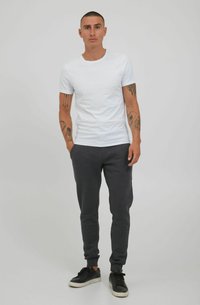 Camiseta blanca de algodón de manga corta combinada con joggers de algodón gris oscuro. Presenta un diseño ajustado y se lleva con zapatillas negras.