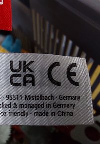 Étiquette en tissu grise avec texte noir comprenant les marquages UKCA et CE, ainsi que des informations sur le produit ; étiquette rouge en haut. Écologique, fabriqué en Chine.