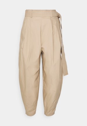 Pantalon beige taille haute effilé avec des plis et une large ceinture en tissu nouée sur le côté droit, présenté sur un fond blanc.