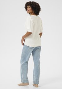 Maglione bianco con texture e maniche a sbuffo, abbinato a jeans a vita alta di colore blu chiaro e scarpe beige con lacci. Un look semplice e casual.