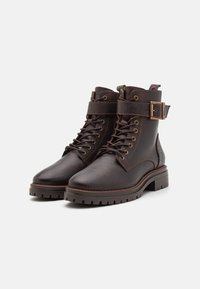 Bottines en cuir marron avec une finition texturée, sangle à boucle en métal, avant lacé et semelle en caoutchouc robuste.