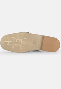Suela de zapato con una superficie de goma texturizada de color beige claro. Presenta un logo elevado y elementos de diseño. Forma robusta y ligeramente curvada.