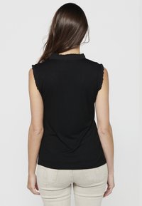 Top nero senza maniche con scollatura e giromanica arricciati. Tessuto morbido, design aderente, visto da dietro su uno sfondo neutro.