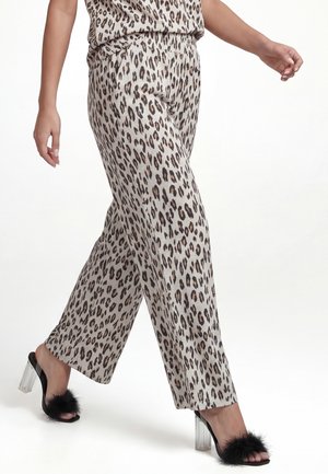 Persona che cammina indossando pantaloni chiari con stampa leopardata e sandali neri con tacco alto, tacchi trasparenti e dettagli in pelliccia nera.