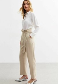 Witte lange mouwen overhemd met knopen, gecombineerd met beige hoge taille broeken met een riem en zijzakken; zilveren puntige schoenen.