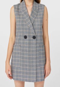 Vestido blazer sin mangas de doble botonadura en un patrón de cuadros grises, con grandes botones negros y dos bolsillos delanteros.
