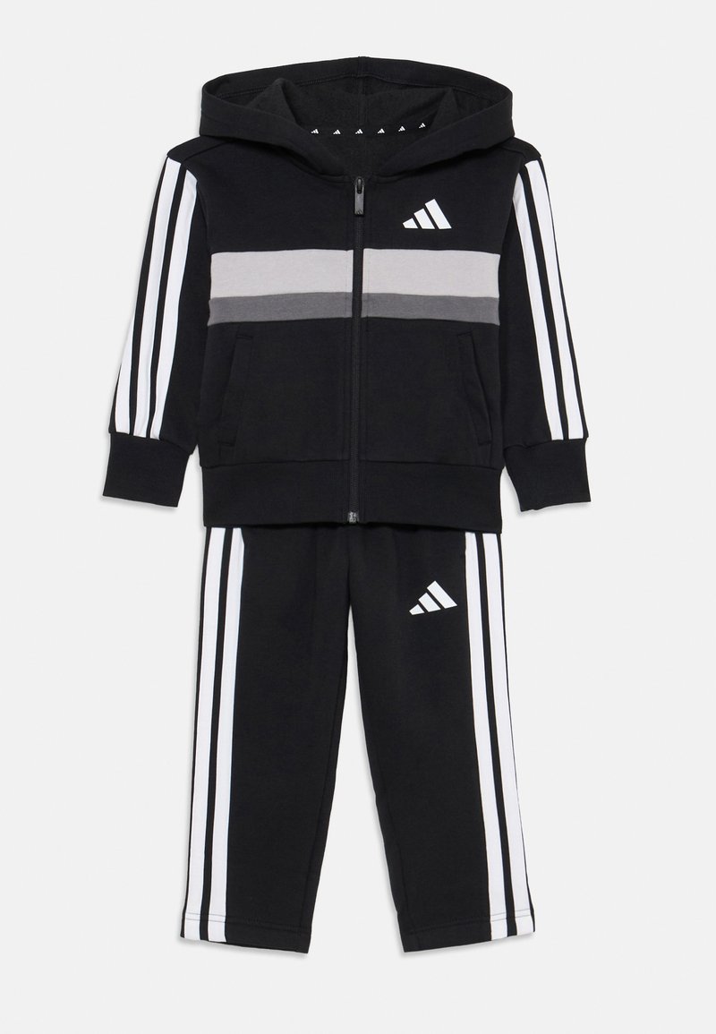 Crni dukserica i trenirke set s bijelim prugama i Adidas logotipom, dizajniran za aktivnu odjeću, prikazan na bijeloj pozadini.