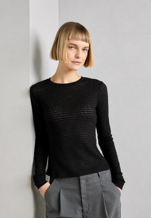 Haut noir à manches longues avec un motif rayé horizontal, fabriqué en matériau léger. Assorti à un pantalon gris taille haute.