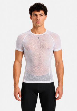 Mann, der nach vorne blickt, trägt ein eng anliegendes weißes Mesh-Kurzarmshirt und schwarze Sporthose vor einem schlichten Hintergrund.