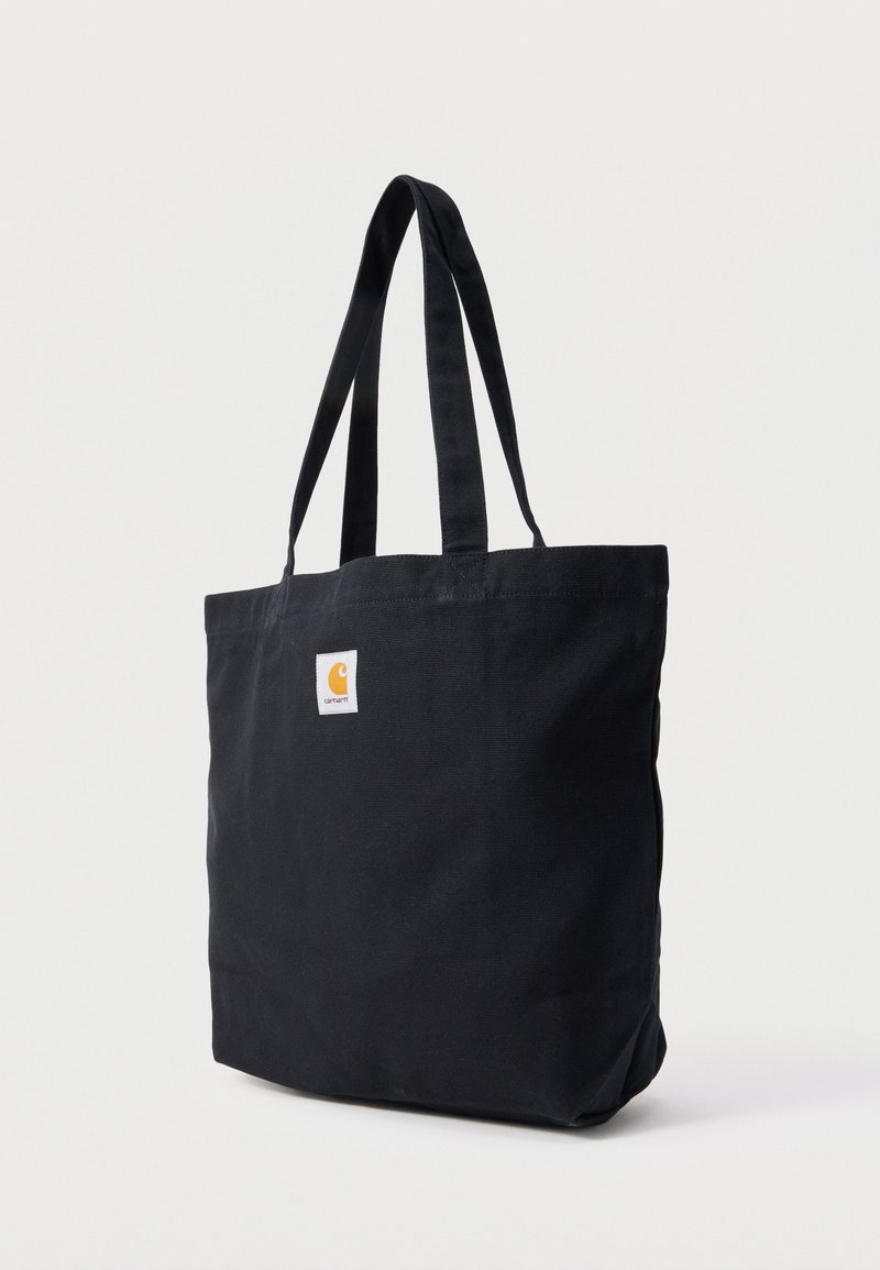 Schwarze Canvas-Tragetasche mit zwei langen Griffen und einem kleinen weißen Logopatch auf der Vorderseite.