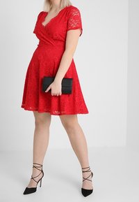 Röd spetsklänning med korta ärmar, knytdesign, utsvängd kjol, kombinerad med svart clutcher och sandaler med hög klack. Slät textur, blommönster.