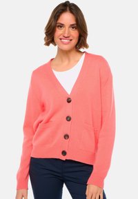 Cardigan en tricot corail avec un col en V, fermeture à boutons sur le devant et deux poches avant. Présente des poignets et un ourlet côtelés. Texture douce, design décontracté.