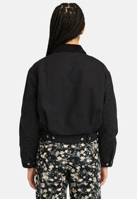 Black cotton blend jacket with a collar, featuring a cropped design and snap-button closure. Paired with floral-patterned pants.