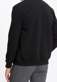 Czarna, teksturowana bluza z gładkim, elastycznym pasem i mankietami. Posiada prosty, okrągły dekolt i dopasowany krój.