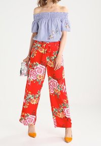 Red floral wide-leg pants with pink and yellow flowers, paired with a blue striped off-shoulder top. Accessories include a small silver bag.