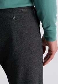 Pantalons noirs texturés avec un motif subtil, dotés d'une poche arrière et d'une étiquette de marque près de la taille. Le tissu semble durable.