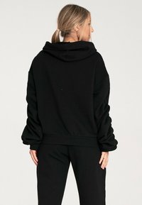 Czarna bluza z kapturem wykonana z miękkiego materiału, z obszernym kapturem, opadającymi ramionami i luźnym krojem. Gładka faktura, minimalistyczny design.