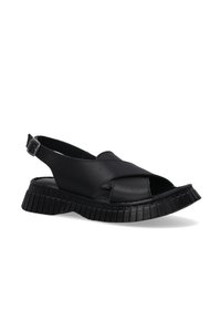 Zwarte slingback sandaal van soepel leer, met een getextureerde rubberen zool met een geribbelde patroon en open teen ontwerp.