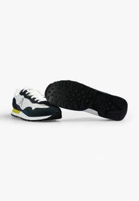 Sneaker bianco e nero con accenti verdi e gialli; materiali in suede e mesh; suola in gomma testurizzata con motivi per migliorare la presa.