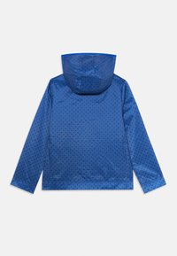 Veste à capuche bleue avec des manches longues et un subtil motif géométrique de triangles sur l'ensemble, vue de dos sur fond uni.