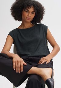 Top nero textured con maniche corte, abbinato a pantaloni neri a gamba larga e scarpe aperte nere, caratterizzati da un design liscio e minimalista.