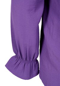 Manche longue violette avec détail de manchette à volant élastiqué sur le tissu.