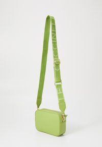 Zelená kožená crossbody taška obdélníkového tvaru. Obsahuje odpovídající texturovaný popruh s detailem loga a zlaté kovové prvky.