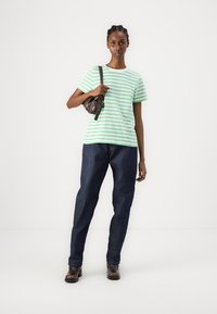 Grønn og hvit stripete t-skjorte kombinert med mørkeblå jeans og brun veske. Modell står oppreist, iført brune ankelstøvler.