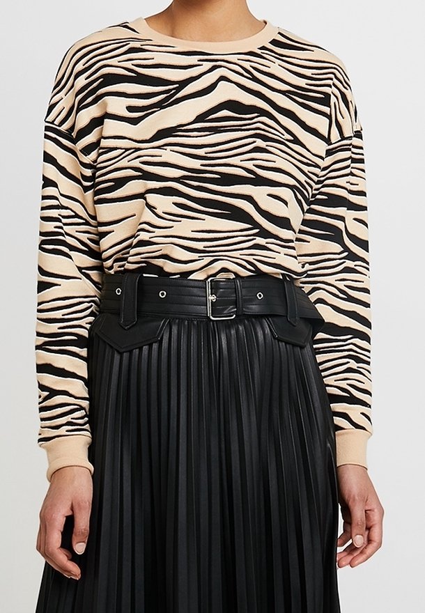 Beige sweatshirt med svarta zebrasträck, matchad med en högmidjad veckad svart läderskjorta och ett svart bälte med silverspänne.