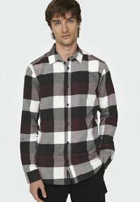 Camisa de manga larga a cuadros con grandes cuadrados en negro, blanco y burdeos. Parte delantera con botones, color clásico y tejido texturizado.