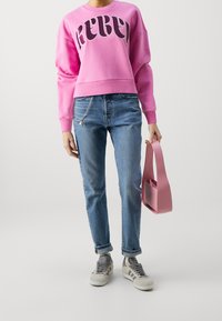 Sudadera rosa con el texto "REBEL", jeans azules, zapatillas gris y blancas, y un bolso rosa. Conjunto casual con un estilo moderno.
