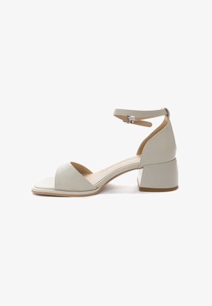 Sandal in pelle grigia chiara con una larga fascia sulla punta, cinturino alla caviglia chiuso da una fibbia argentata e tacco basso a blocco. Texture liscia su tutta la superficie.