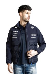 Granatowa bomberka z zamkiem z przodu, kieszeniami z przodu, elastycznymi mankietami i nadrukowanymi logo. Teksturowany materiał o gładkim wykończeniu i wzorze w blokach kolorystycznych.