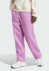 Pantalon de survêtement rose clair en tissu doux, avec une taille élastique et des poches latérales. Détail du logo blanc sur la hanche gauche.