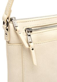 Béžová kožená kabelka s uzatvárateľnou kapsou, striebornými kovovými detailmi a nastaviteľným popruhom. Textúrovaný povrch s kontrastným prešívaním.
